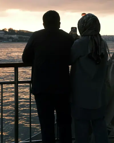 A couple on a ferry at sunset, one of them taking a photo with a phone