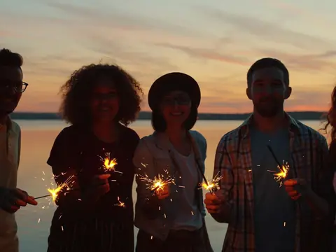 Friends holding sparklers by the water at sunset